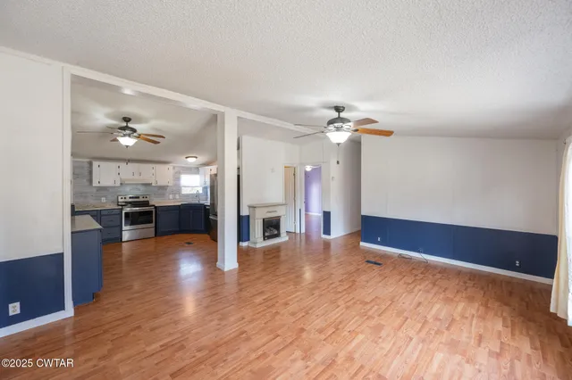 a view of an empty room with wooden floor and a kitchen