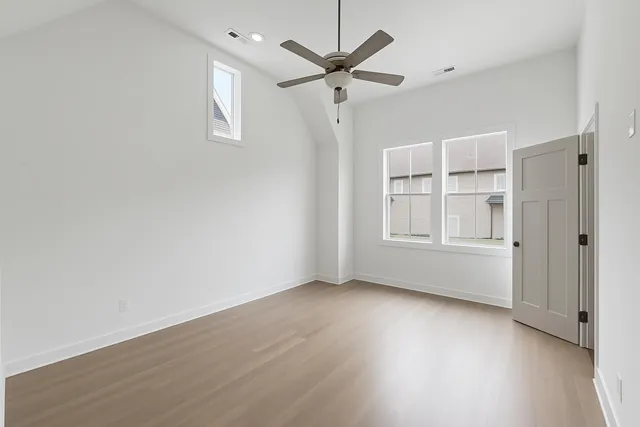 an empty room with wooden floor ceiling fan and windows