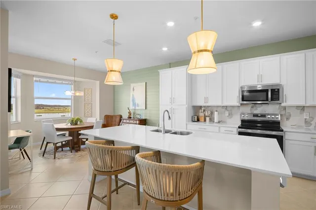 a kitchen with stainless steel appliances granite countertop a sink a stove a kitchen island with chairs and white cabinets