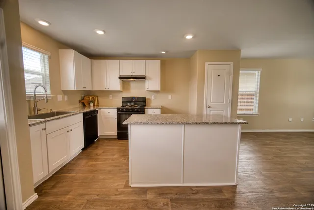 a large kitchen with kitchen island granite countertop a stove a sink a refrigerator and white cabinets with wooden floor