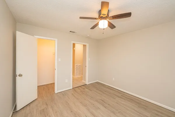 an empty room with wooden floor fan and windows