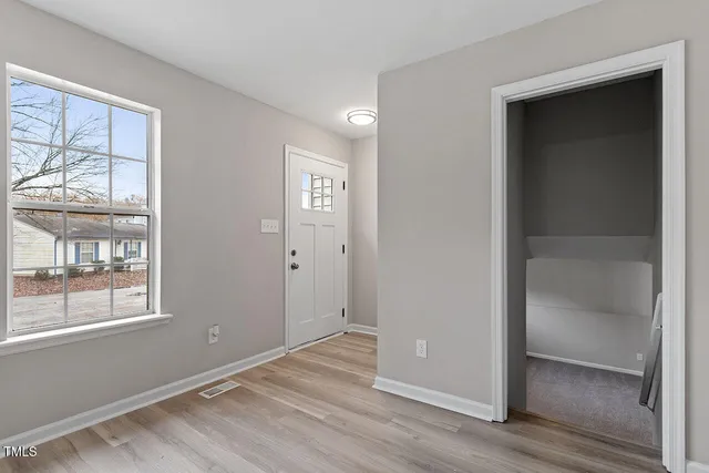 an empty room with wooden floor closet and windows
