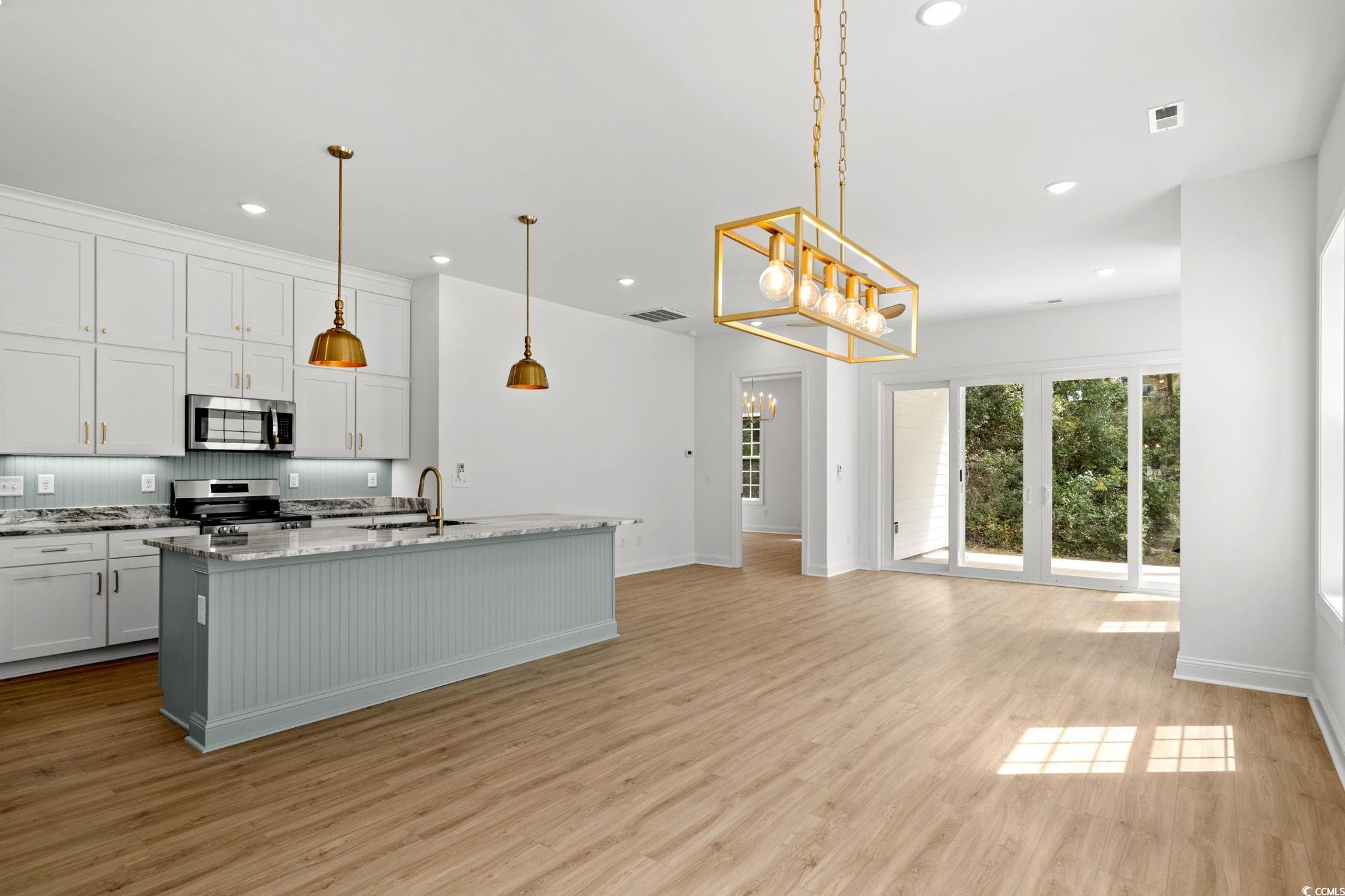 2247 Sand Dunes Drive Myrtle Beach, SC 29577 - Photo 11 of 40 Kitchen featuring a center island with sink, light wood-type flooring, appliances with stainless steel finishes, a chandelier, and light stone countertops