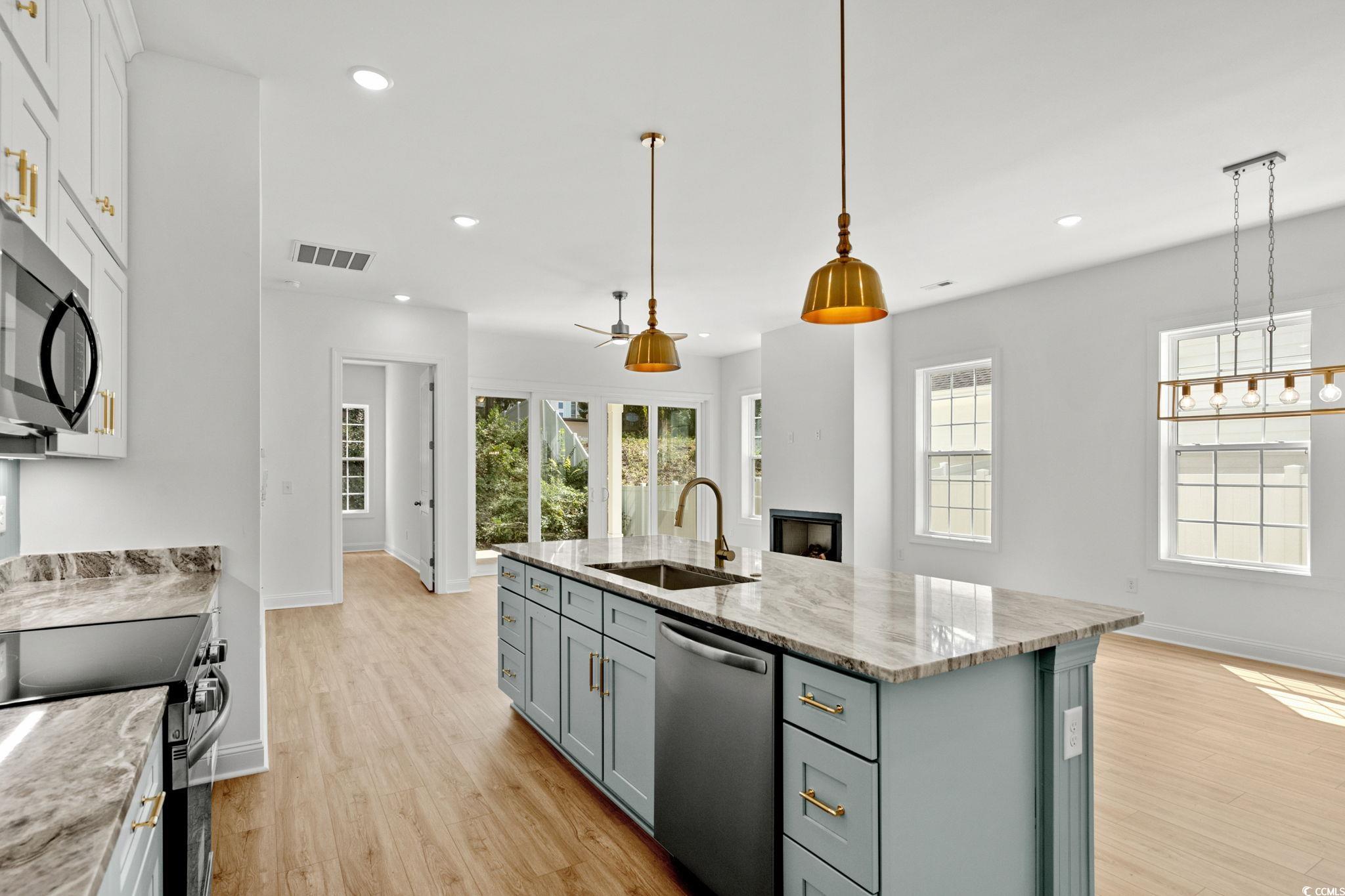 2247 Sand Dunes Drive Myrtle Beach, SC 29577 - Photo 8 of 40 Kitchen with light stone countertops, stainless steel appliances, light wood-style flooring, an island with sink, and decorative light fixtures