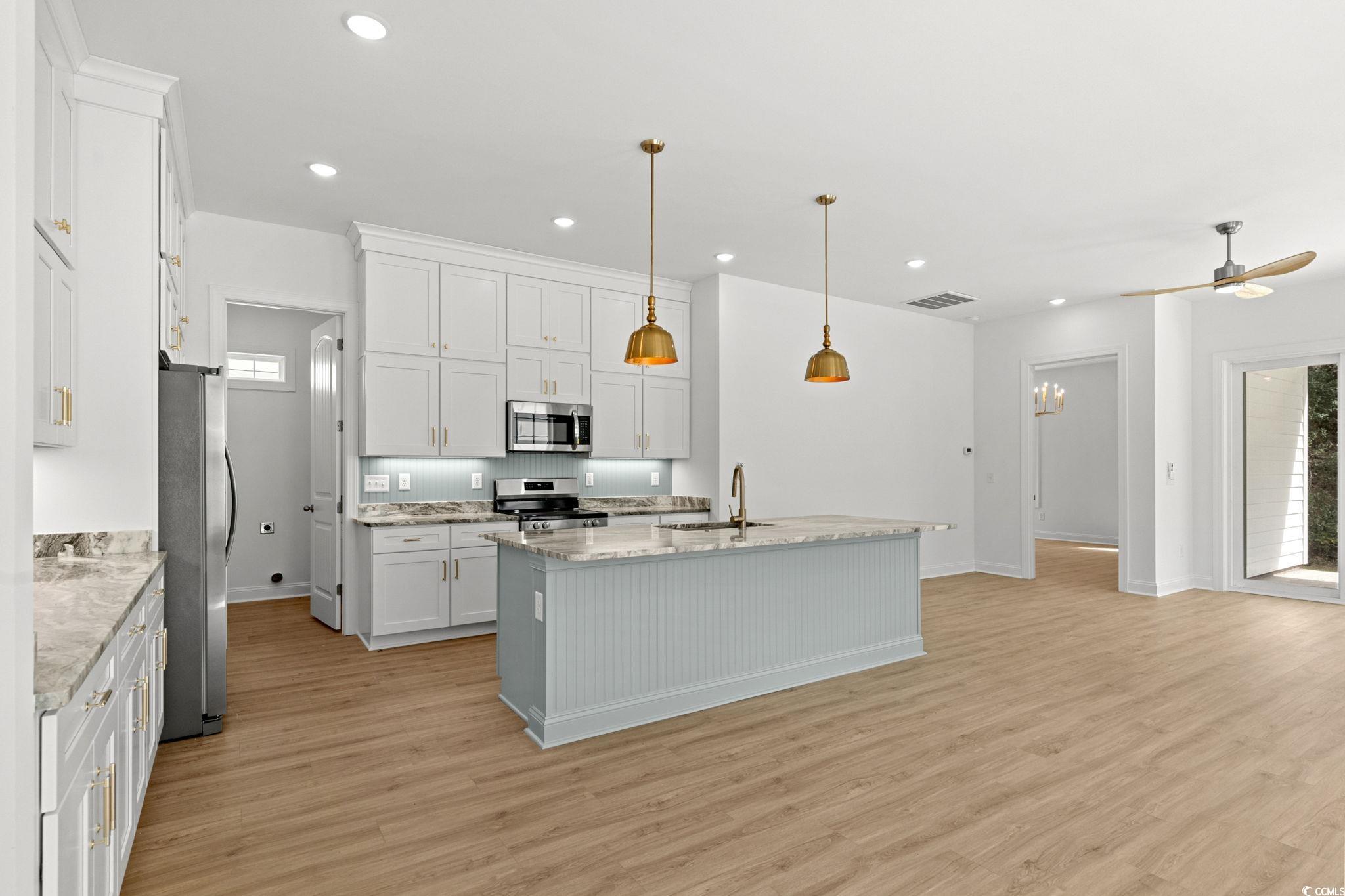 2247 Sand Dunes Drive Myrtle Beach, SC 29577 - Photo 10 of 40 Kitchen with hanging light fixtures, white cabinets, a kitchen island with sink, appliances with stainless steel finishes, and light wood finished floors