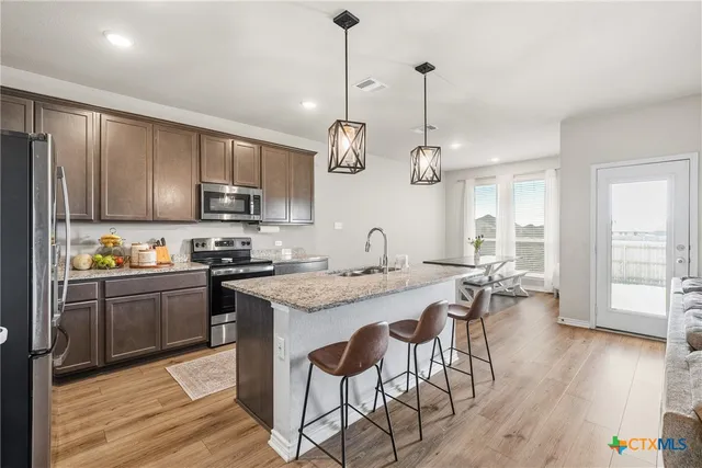 a kitchen with stainless steel appliances granite countertop wooden cabinets a stove a sink a dining table and chairs with wooden floor