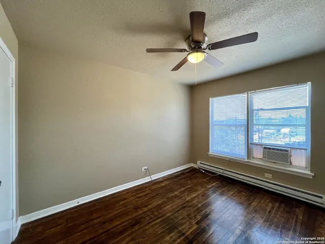 an empty room with wooden floor fan and windows
