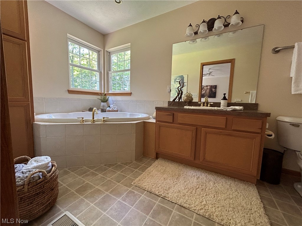 14600 Valentine Road Thompson, OH 44086 - Photo 11 of 31 Bathroom with vanity, tiled tub, a textured ceiling, light tile flooring, and mirror