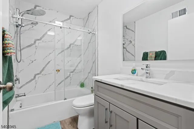 a bathroom with a granite countertop sink a toilet a mirror a vanity a bathtub and shower