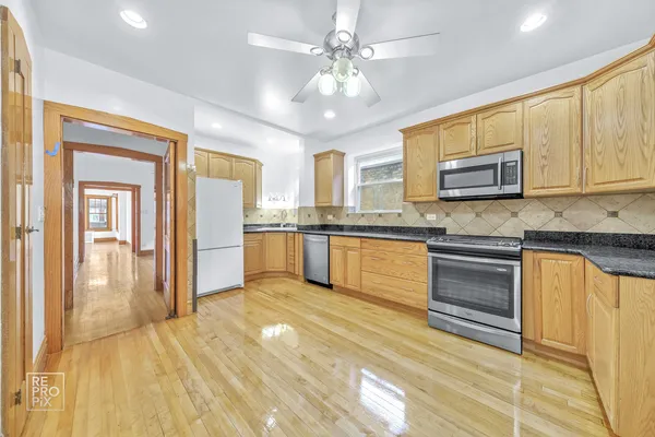 a kitchen with stainless steel appliances granite countertop a stove top oven a sink dishwasher and a refrigerator with wooden floor