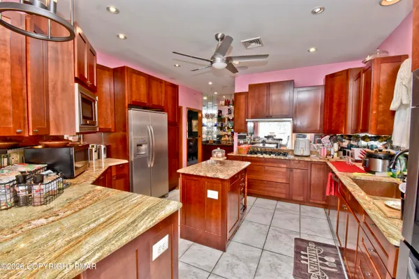 a kitchen with stainless steel appliances kitchen island granite countertop a refrigerator a sink dishwasher and wooden cabinets with a large window