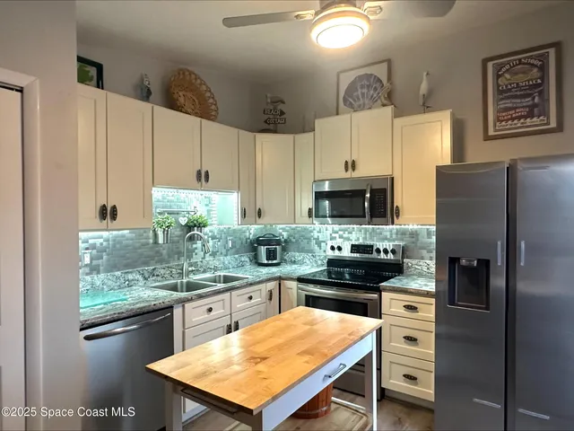 a kitchen with stainless steel appliances kitchen island granite countertop a refrigerator a stove a sink dishwasher and white cabinets with wooden floor