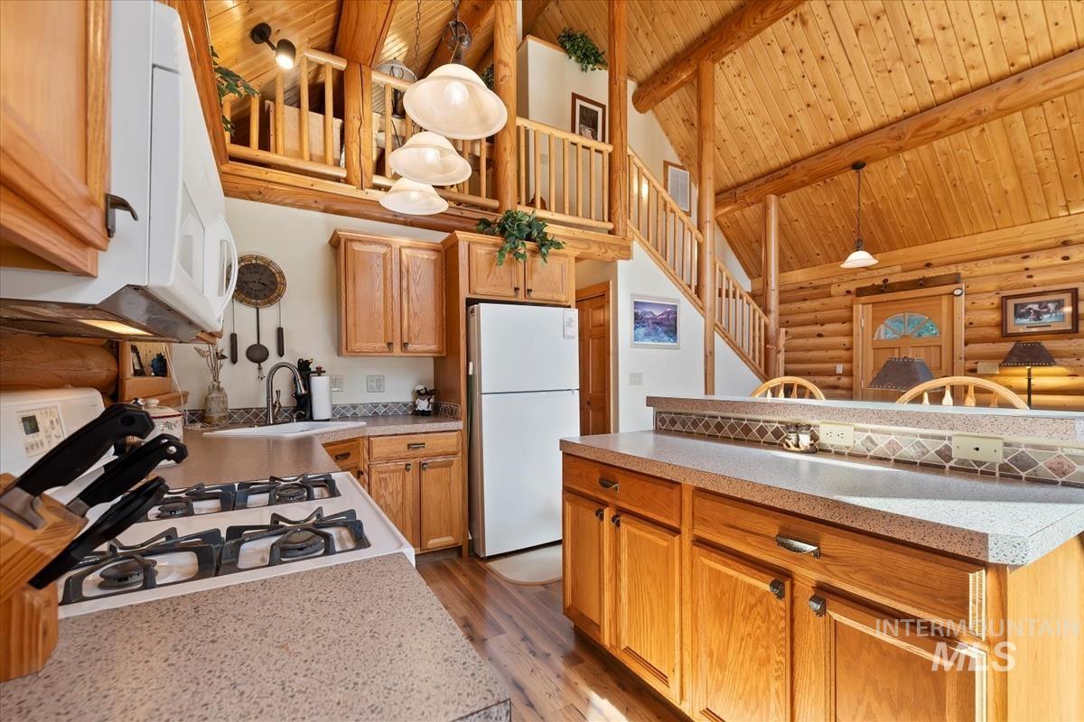 10 Elk Point Road Garden Valley, ID 83622 - Photo 17 of 42 Kitchen with rustic walls, white appliances, light countertops, hanging light fixtures, and a high wood beamed ceiling
