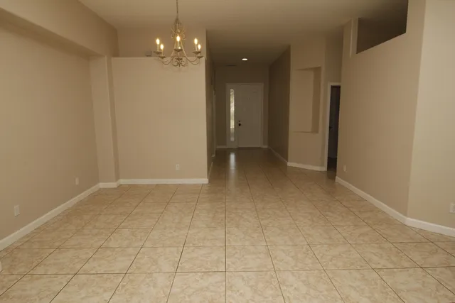 a view of an empty room with chandelier fan and kitchen view