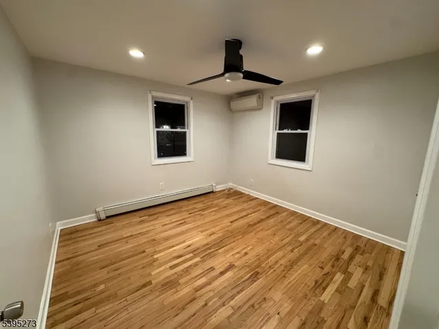 an empty room with wooden floor ceiling fan and windows