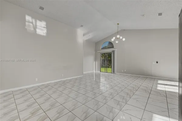 a view of an empty room with window and chandelier fan