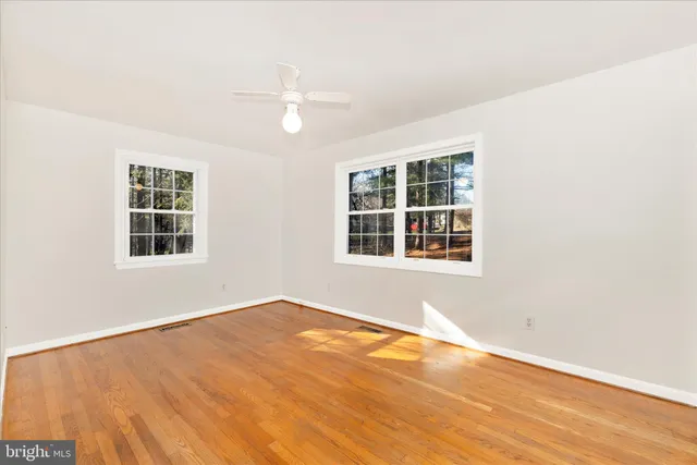 an empty room with wooden floor fan and windows
