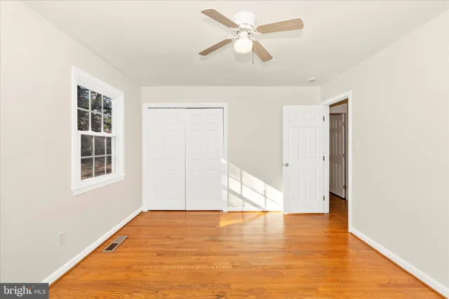 a view of an empty room with wooden floor and a ceiling fan