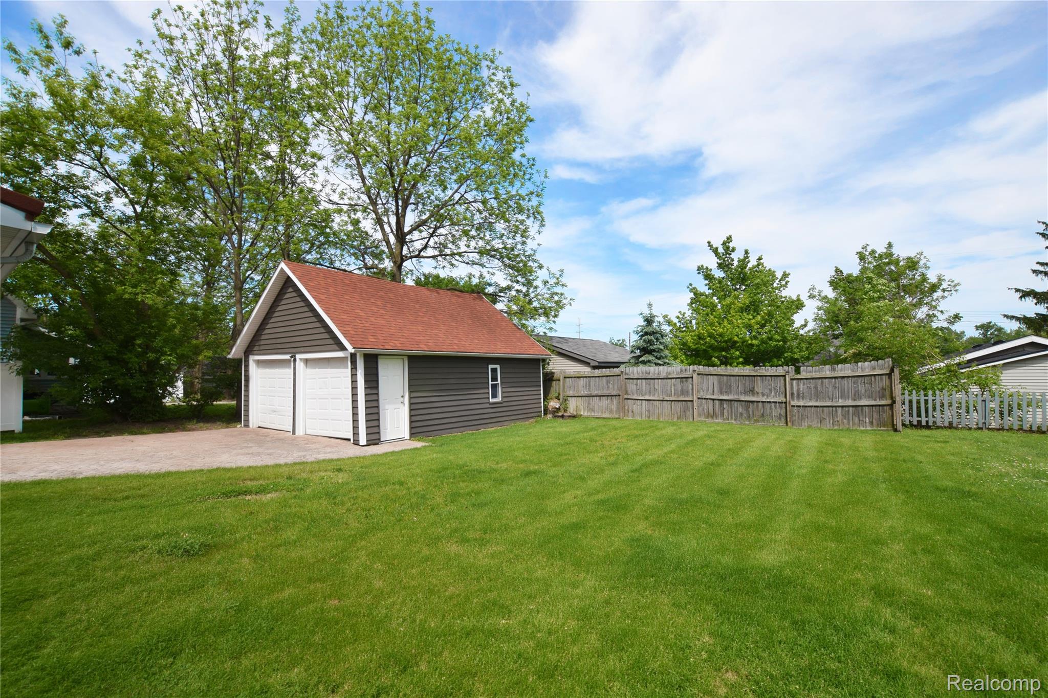 404 North Adelaide Street Fenton, MI 48430 - Photo 21 of 23 Detached two-car garage with a red shingle roof and brown siding, featuring two white garage doors and a side entry door