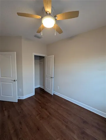 a view of an empty room with wooden floor and a ceiling fan
