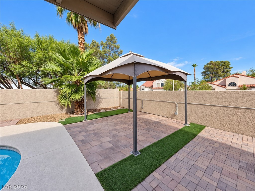 43 Bayridge Road Henderson, NV 89074 - Photo 7 of 47 An inviting backyard patio features classic pavers alongside a shaded canopy and lush palm trees.