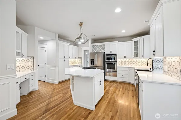 a large kitchen with stainless steel appliances kitchen island granite countertop a large counter top a sink dishwasher a refrigerator and white cabinets with wooden floor