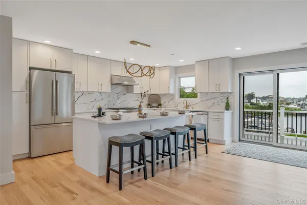 a kitchen with stainless steel appliances granite countertop a refrigerator a sink dishwasher a stove and white cabinets with wooden floor