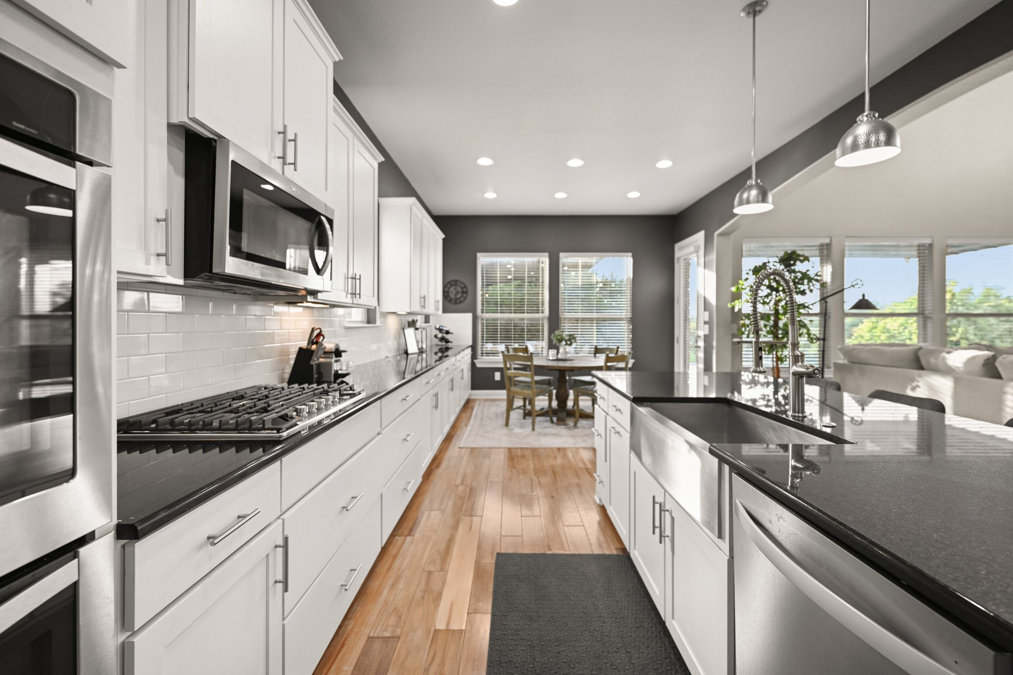 22524 Rock Wren Road Spicewood, TX 78669 - Photo 14 of 40 Modern kitchen featuring white cabinetry, dark countertops, wood-finish flooring, stainless steel appliances, and a farmhouse sink