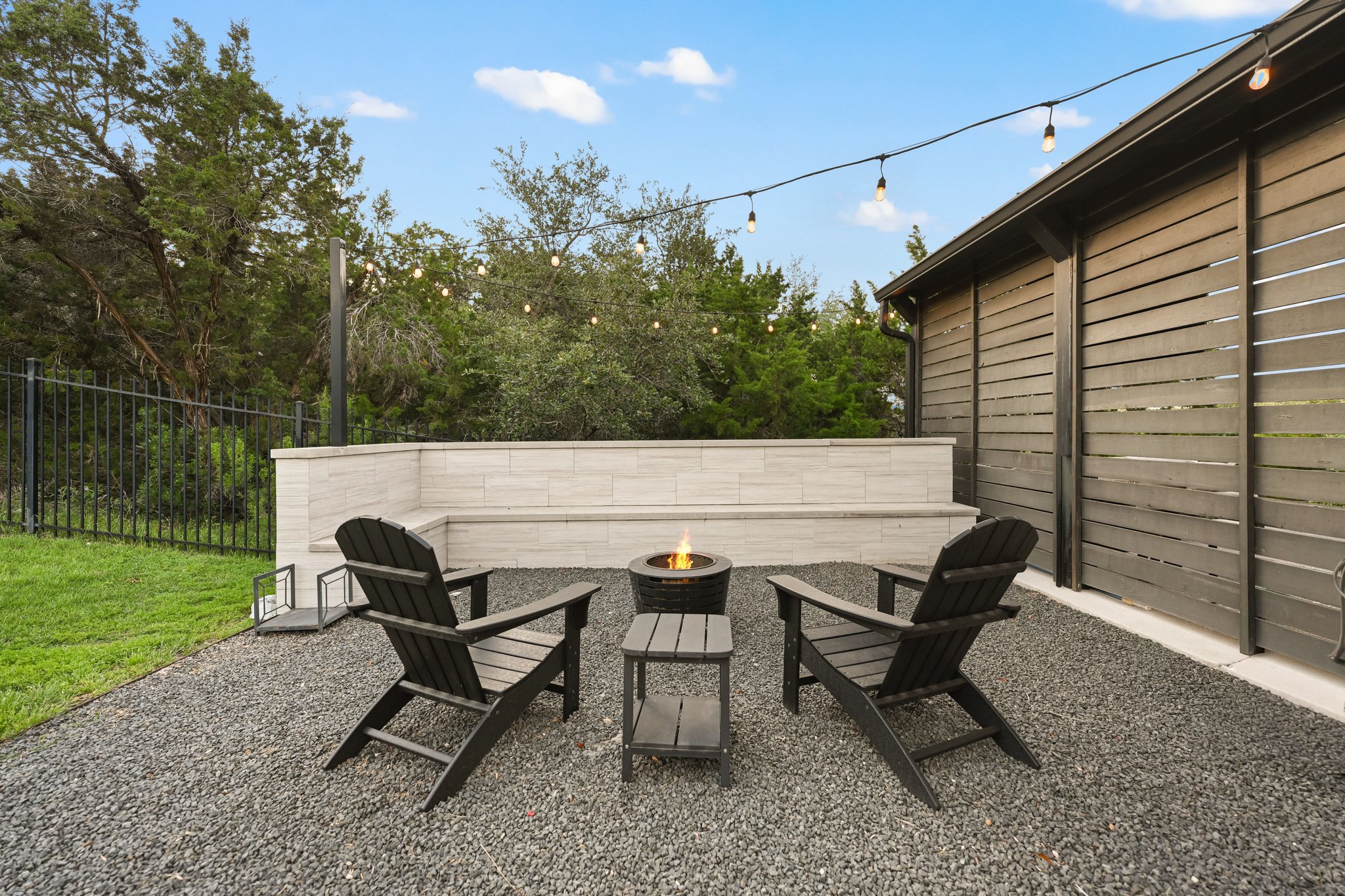 22524 Rock Wren Road Spicewood, TX 78669 - Photo 32 of 40 Outdoor patio featuring a gravel surface, built-in stone bench, string lighting, and a slatted privacy wall