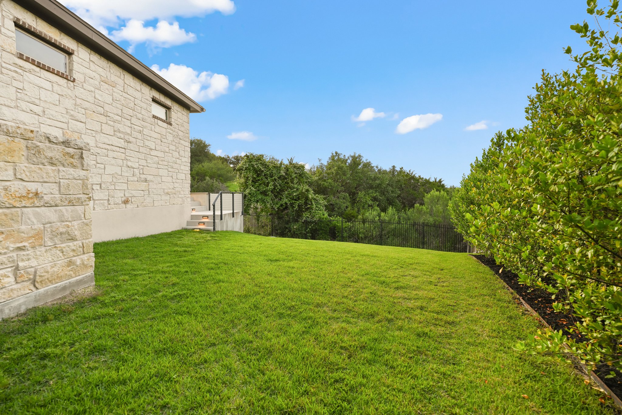22524 Rock Wren Road Spicewood, TX 78669 - Photo 34 of 40 Expansive green lawn bordering a stone-clad exterior with a perimeter fence