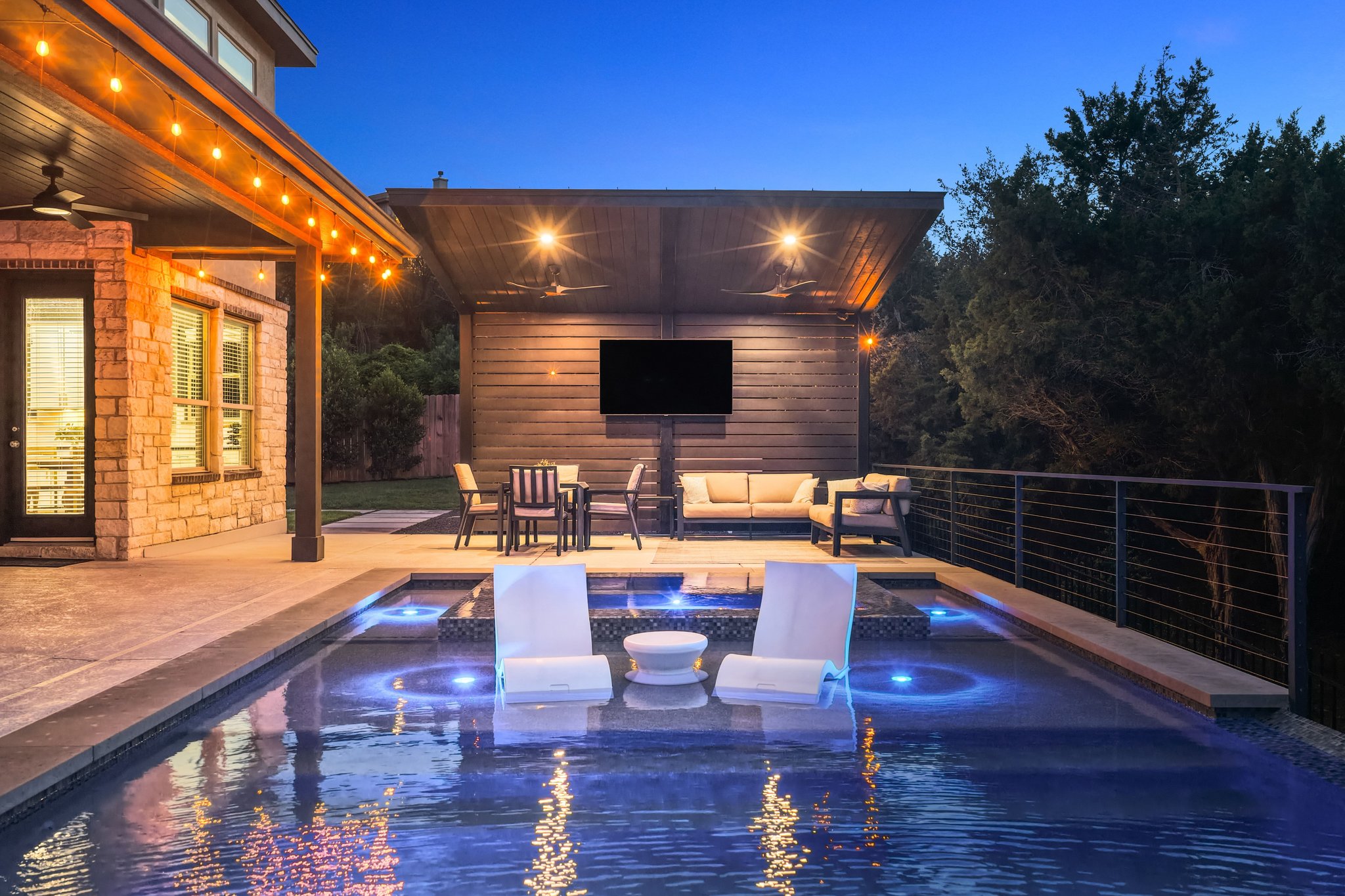 22524 Rock Wren Road Spicewood, TX 78669 - Photo 36 of 40 Luminous outdoor living space featuring a swimming pool with integrated spa, a cable railing system, a covered patio with string lights, and an additional covered outdoor area with a built-in television