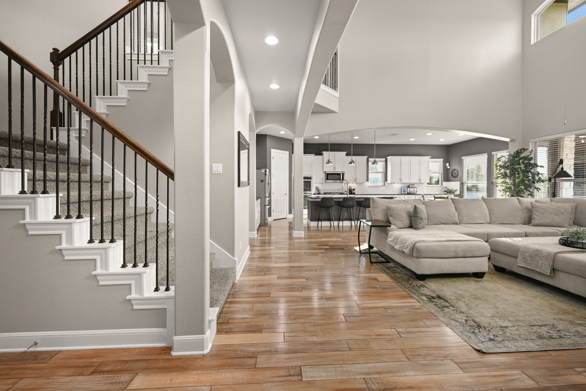 22524 Rock Wren Road Spicewood, TX 78669 - Photo 4 of 40 Two-story living area featuring hardwood flooring, a grand staircase with wrought iron balusters, recessed lighting, and a kitchen with an island and pendant lighting