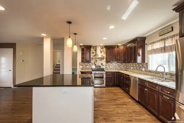 a large kitchen with stainless steel appliances kitchen island granite countertop a stove a sink a refrigerator and a granite countertops with wooden floor