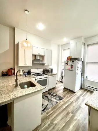 a kitchen with a stove a sink dishwasher a refrigerator and white cabinets with wooden floor