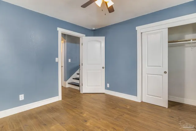 a view of an empty room with wooden floor closet and a ceiling fan
