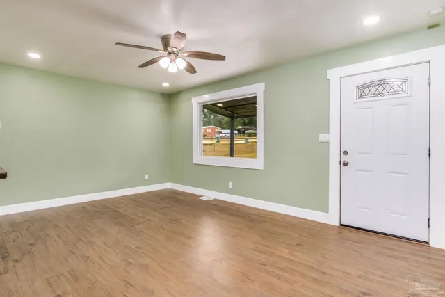 an empty room with wooden floor ceiling fan and windows