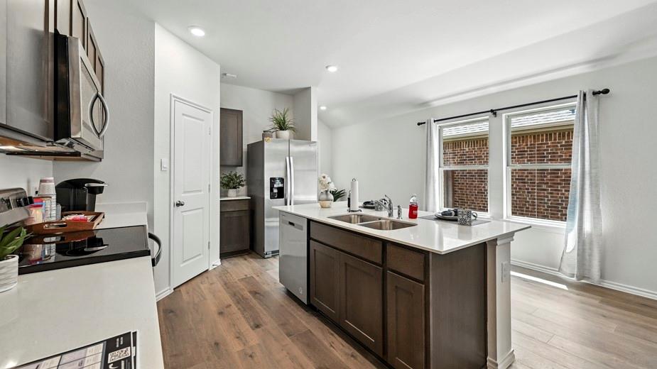 646 Glee Stem Road Lavon, TX 75166 - Photo 4 of 17 Open-concept kitchen featuring an island with a dual-basin sink, stainless steel appliances, wood-finish flooring, and ample natural light from multiple windows