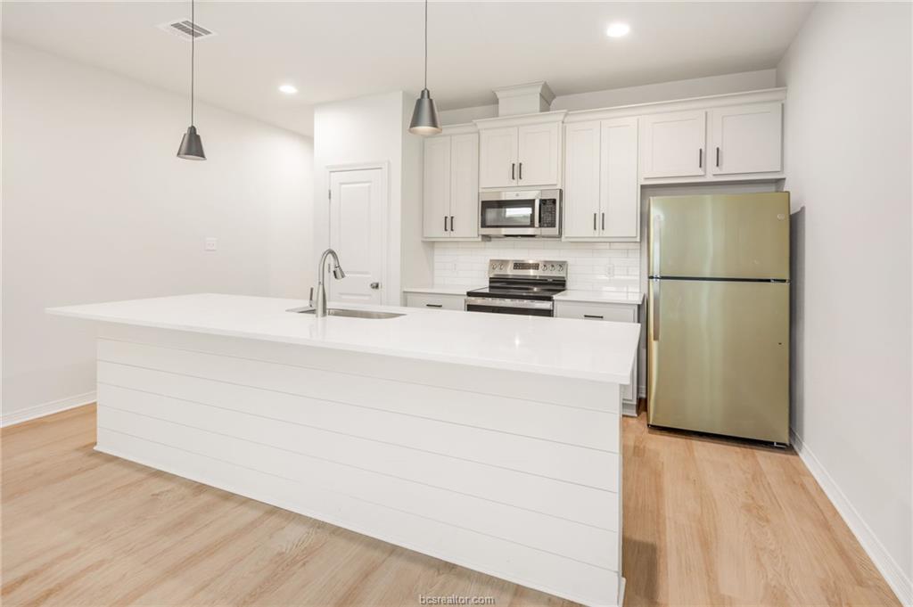 607 Highlands Street, Unit A College Station, TX 77840 - Photo 11 of 19 a kitchen with kitchen island a white counter top space a refrigerator cabinets and a wooden floor
