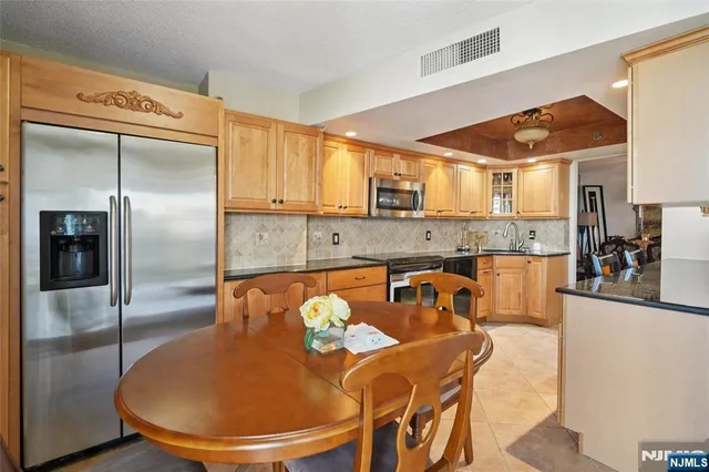 a kitchen with stainless steel appliances granite countertop a refrigerator a sink a dining table and chairs with wooden floor