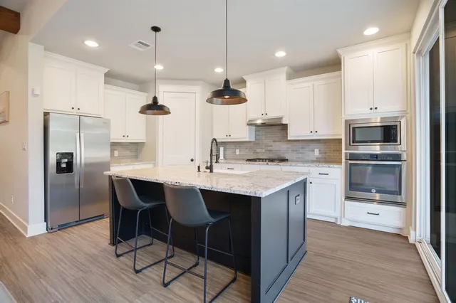 a kitchen with stainless steel appliances kitchen island granite countertop a sink a stove a refrigerator and island with wooden floor