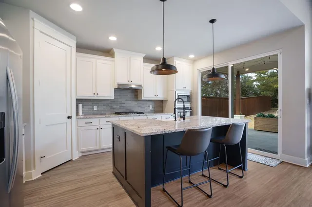 a kitchen with stainless steel appliances granite countertop a sink a stove a refrigerator and island with wooden floor