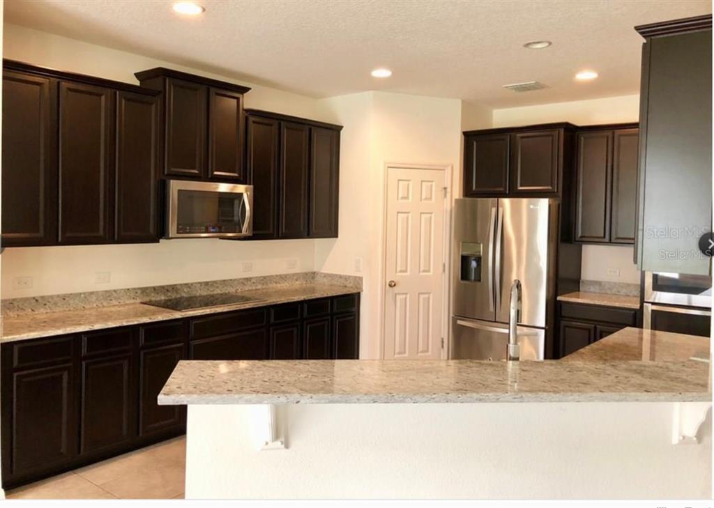 14903 Fells Lane Orlando, FL 32827 - Photo 4 of 14 a kitchen with granite countertop a refrigerator and a stove top oven