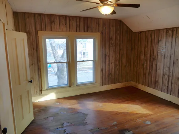 an empty room with wooden floor fan and windows