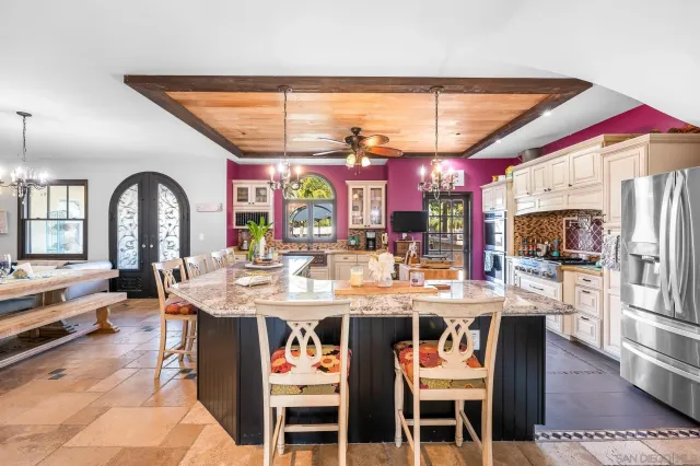 a room with stainless steel appliances kitchen island granite countertop a dining table and chairs a refrigerator with wooden floors