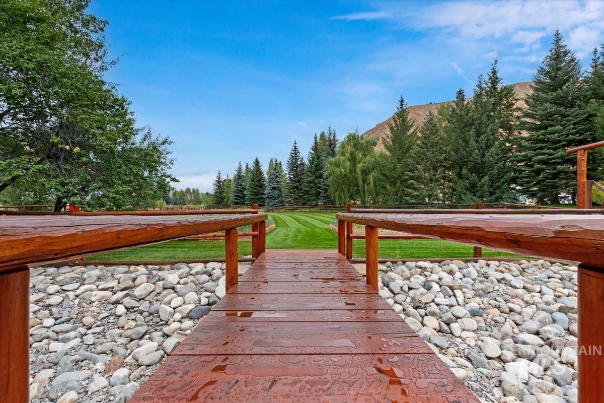 106 Hidden Hollow Road Hailey, ID 83333 - Photo 14 of 49 Wood-finish decking with railings, river rock landscaping, and a manicured lawn framed by mature evergreen trees