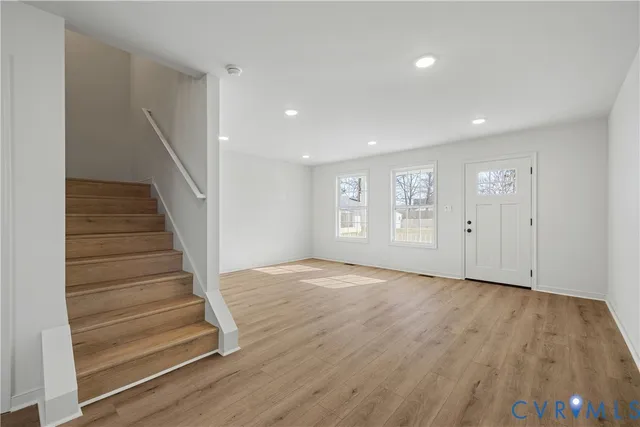 a view of an empty room with wooden floor and stairs
