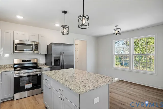 a kitchen with kitchen island granite countertop a stove top oven a refrigerator cabinets and wooden floor