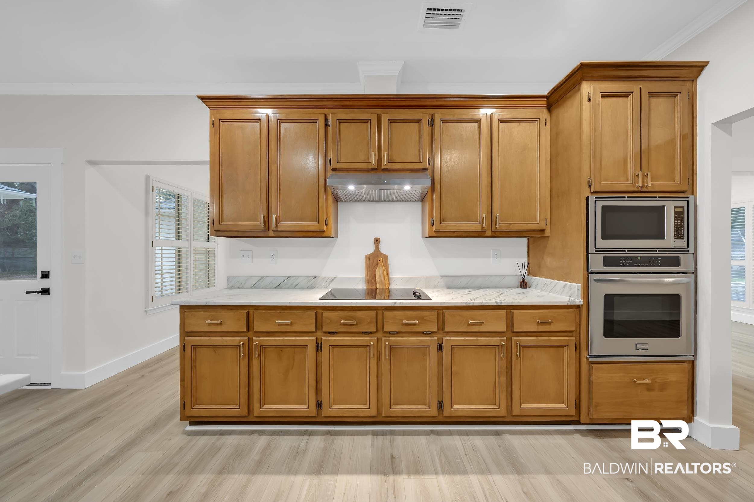 4924 Brooke Court Mobile, AL 36618 - Photo 15 of 34 Kitchen featuring brown cabinets, appliances with stainless steel finishes, ornamental molding, under cabinet range hood, and light wood-type flooring