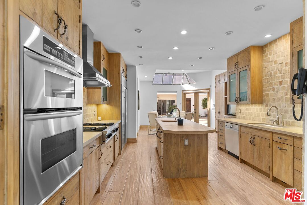 605 North Hillcrest Road Beverly Hills, CA 90210 - Photo 6 of 36 a kitchen with stainless steel appliances granite countertop a refrigerator a stove oven and white cabinets with wooden floors