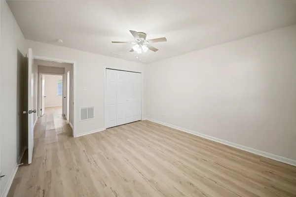an empty room with wooden floor fan and windows
